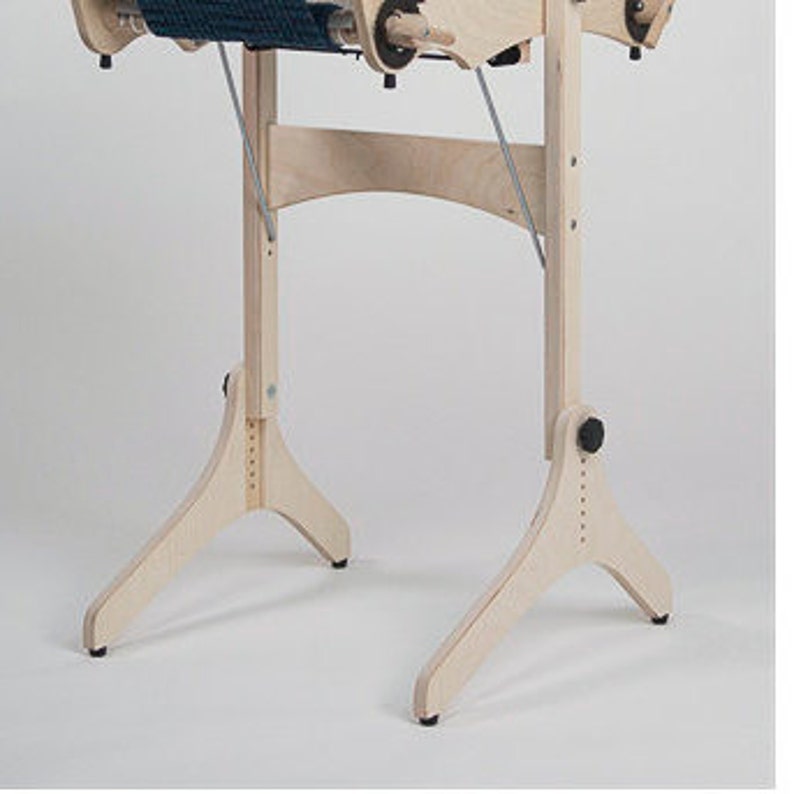 以下が含まれることがあります： 三角形のベースと高さ調節可能な木製織機スタンド。スタンドは天然木で作られており、薄い茶色の仕上げになっています。