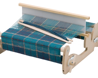 May include: A wooden loom with a blue and red plaid fabric woven on it. The loom has two wooden sticks for weaving and a crank on the side.