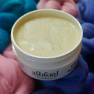 Puede incluir: Un tarro de pl&aacute;stico blanco con tapa transparente que contiene una sustancia blanca y cremosa. El tarro est&aacute; etiquetado con "Ashford" y "Wool Wax".