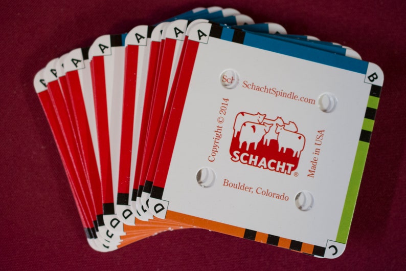 Puede incluir: Un abanico de tarjetas Schacht Spindle, con fondo blanco y bordes rojos y naranjas. Las tarjetas muestran el logotipo de Schacht, el sitio web y el texto "Made in USA". Las tarjetas est&aacute;n etiquetadas con las letras A, B, C y D.