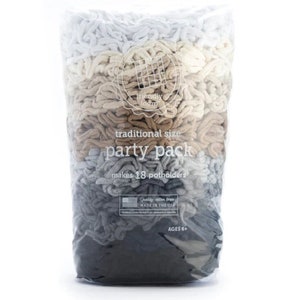 Op de afbeelding: Een doorzichtige plastic zak gevuld met lussen garen in verschillende tinten grijs, bruin en wit. De zak is gelabeld "traditionele maat feestpakket" en "maakt 18 ovenwanten".