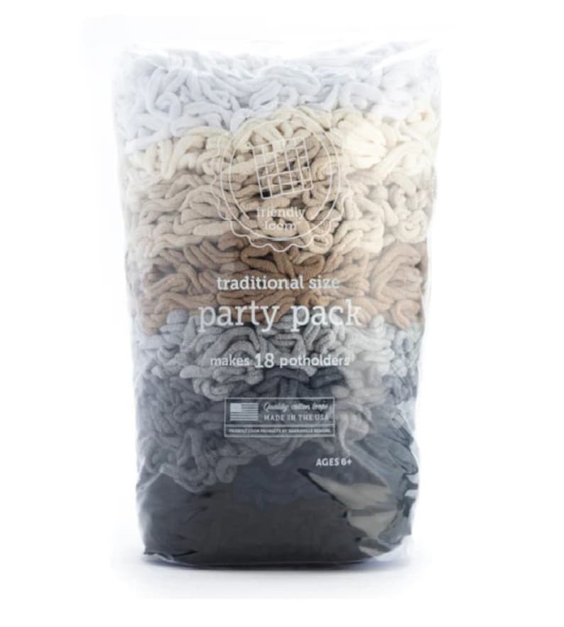 Op de afbeelding: Een doorzichtige plastic zak gevuld met lussen garen in verschillende tinten grijs, bruin en wit. De zak is gelabeld "traditionele maat feestpakket" en "maakt 18 ovenwanten".