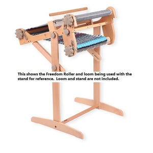 May include: A wooden loom stand with a Freedom Roller attached. The loom stand is made of natural wood and has a simple design. The Freedom Roller is a device used to help weave fabric.