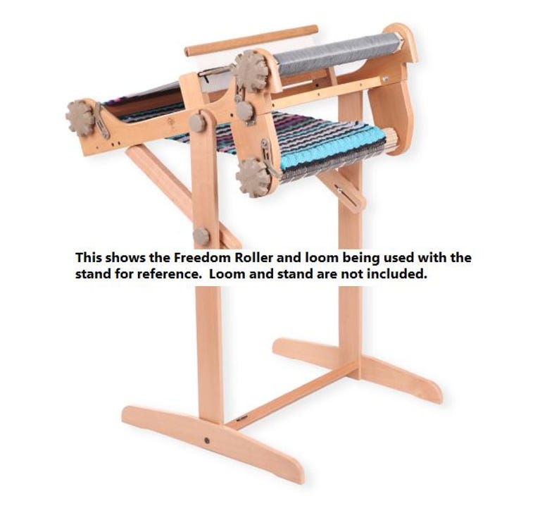 May include: A wooden loom stand with a Freedom Roller attached. The loom stand is made of natural wood and has a simple design. The Freedom Roller is a device used to help weave fabric.