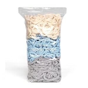 May include: A clear plastic bag filled with cotton loops in three colors: cream, light blue, and gray. The bag has the text "friendly loom" and "pro size cotton loops" printed on it. The loops are for making 6 potholders.