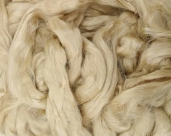 May include: Close-up of a pile of raw, undyed flax fiber. The fibers are a light beige color, with variations in tone. The texture appears soft and slightly wavy, suggesting it is ready for spinning or other textile uses.