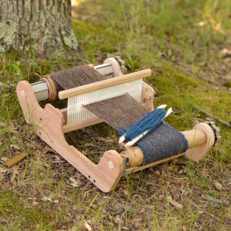 May include: A wooden loom with brown and blue yarn being woven. The loom has two spools, one with brown yarn and the other with a blue and brown patterned fabric.