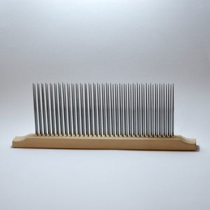 May include: A wooden comb with a row of metal teeth. The comb is used for grooming wool.