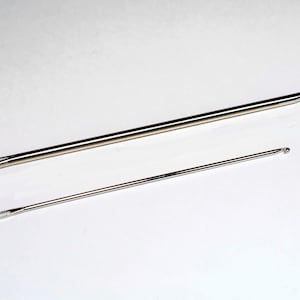 May include: Two silver crochet hooks, one larger than the other, on a white background.