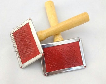 May include: Two red and silver pet grooming brushes with wooden handles. The brushes have a rectangular shape and are made of metal with a red rubber backing. The handles are made of natural wood.