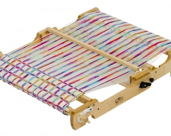 Könnte beinhalten: Ein Holzwebstuhl mit einem bunten gewebten Stoff darauf. Der Webstuhl hat einen Holzrahmen und einen Holzschützen. Der Stoff ist mit einer Vielzahl von Farben gewebt, darunter Rosa, Lila, Blau, Grün und Gelb.