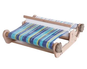 May include: A wooden loom with a blue, green, and white striped fabric woven on it. The loom has two wooden spools and a wooden shuttle.