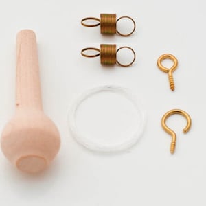 May include: A set of wooden finials, two gold spring hooks, two gold eye hooks, and a clear string. The finials are light brown and have a rounded shape.