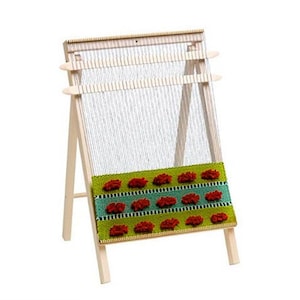May include: A wooden loom with a green and blue woven tapestry with red pom-poms. The loom is on a stand with two legs.