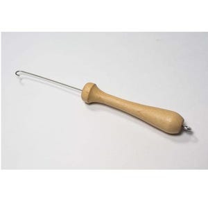 May include: A wooden yarn winder with a metal hook. The winder is light brown and has a smooth finish. The hook is attached to the end of the winder and is bent into a loop.