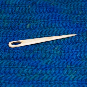 Puede incluir: Una aguja de madera con un peque&ntilde;o agujero en un extremo, que se encuentra sobre una superficie azul y peluda.