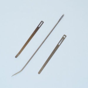 May include: Three metal needles with eye holes for threading. The needles are different lengths and have a silver finish.
