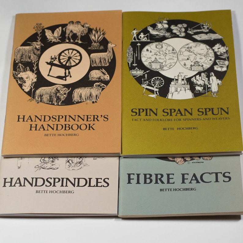 Puede incluir: Cuatro libros con cubiertas marrones, verdes, beige y azules. Los libros se titulan "Handspinner's Handbook", "Spin Span Spun", "Handspindles" y "Fibre Facts". Todos los libros tienen el nombre del autor, Bette Hochberg, impreso en la portada.