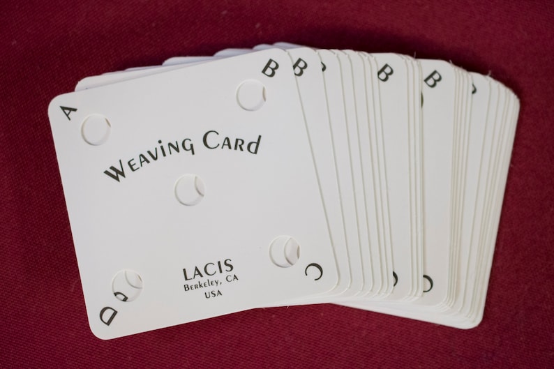 Puede incluir: Un mont&oacute;n de tarjetas de tejido blancas con esquinas redondeadas, con el texto "Weaving Card" y la marca "LACIS". Cada tarjeta tiene cuatro recortes circulares y est&aacute; marcada con las letras A, B, C y D. Las tarjetas est&aacute;n sobre una superficie roja.