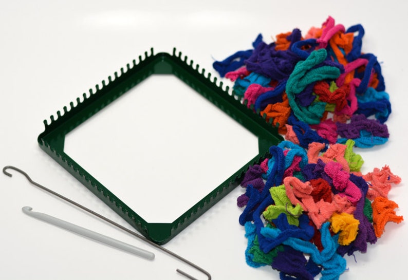 May include: A green plastic loom with a hook and a pile of colorful yarn scraps.