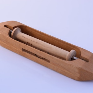 May include: A wooden yarn swift with a spindle for winding yarn. The swift is made of light brown wood and has a smooth finish. The spindle is made of natural wood and has a small knob on one end.