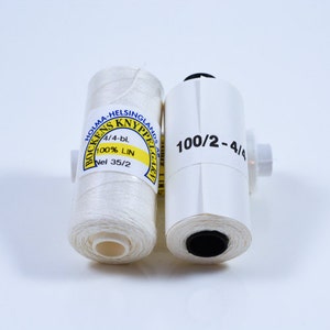May include: Two spools of white linen thread for bobbin lace making. The spool on the left has a yellow label with the text "Bockens Knyppelgarn Holma-Helsingland 4/4-bl. 100% LIN Nel 35/2". The spool on the right has a white label with the text "100/2-4/4".