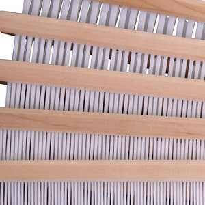 May include: A wooden loom with white warp threads. The loom has four wooden bars with a white string running through each bar.