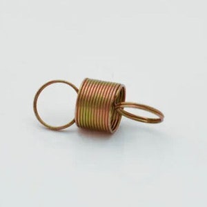 May include: A gold-colored spring with a loop on each end. The spring is coiled tightly and appears to be made of metal.