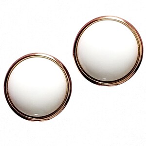 May include: A pair of round, white earrings with a gold-colored metal border. The earrings have a simple, classic design, and are set against a white background.