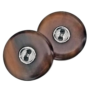 May include: Two round, brown buttons with a marbled effect. Each button has a silver-colored metal shank with two holes for sewing. The buttons are a classic design, suitable for various sewing projects.