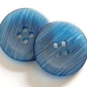 May include: Two blue plastic buttons with four holes each. The buttons have a textured, brushed finish.