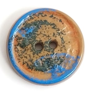 May include: A two-hole ceramic button with a brown, orange, and blue speckled design. The button has a blue rim.