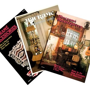 May include: Three vintage macrame pattern books with colorful covers. The covers feature macrame projects, including a hanging plant holder, a spiral staircase, and a lion's cradle. The titles of the books are "Macrame Accessories", "Macrame For Everyday Living", and "Macrame Masterpieces".