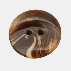 May include: A round button with two holes, featuring a marbled pattern in shades of brown, tan, and cream. The button has a glossy finish and is suitable for sewing projects. The button's diameter is approximately 1 inch.