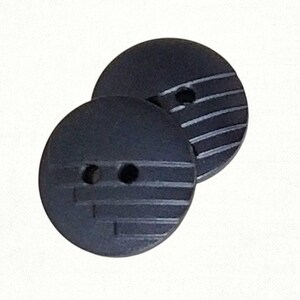 May include: Two black, round buttons with a textured, striped design. Each button has two holes for sewing. The buttons are made of a solid, dark material.