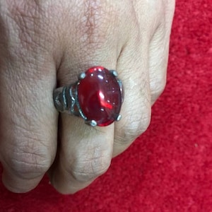 Può includere: Un anello d'argento con una grande pietra rossa di forma ovale.