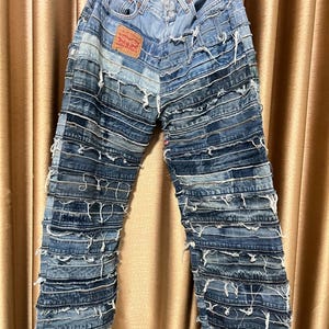 Può includere: Jeans in denim blu con più strati di denim cuciti, creando un aspetto stratificato e testurizzato. I jeans hanno uno stile classico a cinque tasche e una gamba dritta.