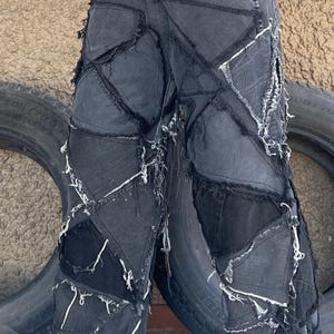 Puede incluir: Pantalones de mezclilla negros con múltiples parches y bordes deshilachados. Los pantalones están hechos de un mosaico de diferentes telas de mezclilla.