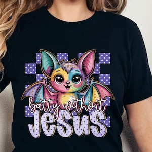 May include: Black t-shirt featuring a colorful cartoon bat with the text "batty without JESUS". The bat has large eyes and multi-colored wings. The background includes a purple and white checkered pattern.