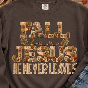 May include: A dark brown crewneck sweatshirt featuring a graphic with the text FALL FOR JESUS HE NEVER LEAVES. The letters are filled with a patchwork pattern of autumn leaves, pumpkins, and plaid designs in orange, yellow, and brown tones.