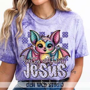 May include: Purple tie-dye t-shirt featuring a colorful cartoon bat with large eyes and wings. The text "batty without JESUS" is below the bat. The shirt has a crew neck and short sleeves.