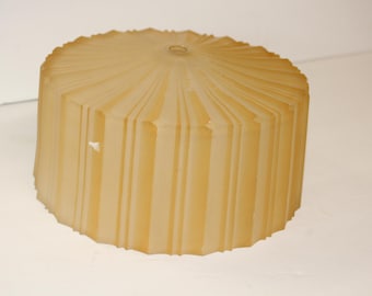 May include: A cylindrical, frosted glass lampshade with a pleated design. The shade is a warm, amber color and has a small hole at the top. The vertical pleats create a textured surface. The lampshade is likely for a vintage or retro-style lamp.