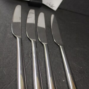 May include: Four silver dinner knives with a polished finish. The knives are arranged in a row, with the handles pointing to the right.