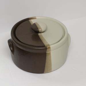 May include: A brown and white ceramic casserole dish with a lid. The dish has two handles and a brown and white striped design.