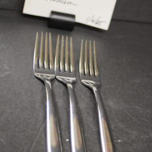 May include: Three silver forks with a polished finish. The forks are arranged in a row, with the tines facing up.