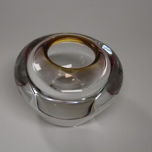 May include: A clear glass decorative bowl with a circular opening and a rounded shape. The bowl has a gradient of colors, transitioning from a golden-brown hue at the top to a clear base. The design is modern and minimalist.