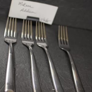 May include: Four silver forks with a polished finish. The forks are arranged in a row on a dark gray surface.