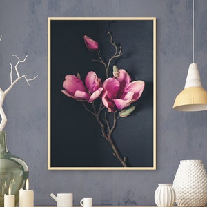 May include: A wooden table with two trestle legs, a wicker basket, a green glass vase, and a framed print of pink magnolia flowers on a dark background.