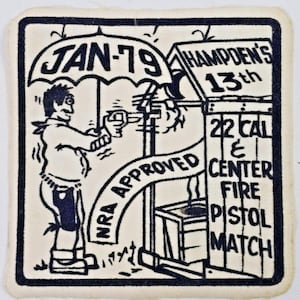 Può includere: Una toppa vintage con un'illustrazione a fumetti in bianco e nero. Raffigura una figura che spara con una pistola sotto un ombrello con la scritta "JAN-79". Il testo include "Hampden's 13th", "22 Cal & Center Fire Pistol Match" e "NRA Approved".