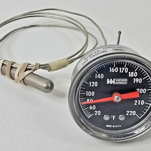 Può includere: Un termometro a quadrante argentato con un quadrante nero e un ago rosso. Il termometro legge da 20 a 220 gradi Fahrenheit. Il termometro ha una sonda con un filo argentato collegato ad essa. Il termometro è etichettato "WI WEISS INSTRUMENTS" e "MODEL KIU 01-2015".